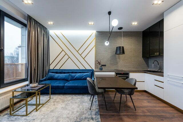 Nowoczesny salon z kuchnią, minimalistyczny wystr&oacute;j, wygodna sofa i nowoczesne oświetlenie.
